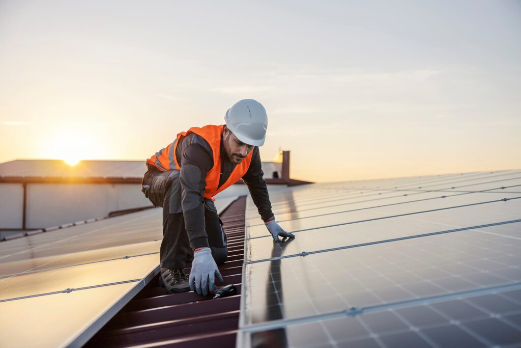 A person in a vest and white helmet working on solar panels.